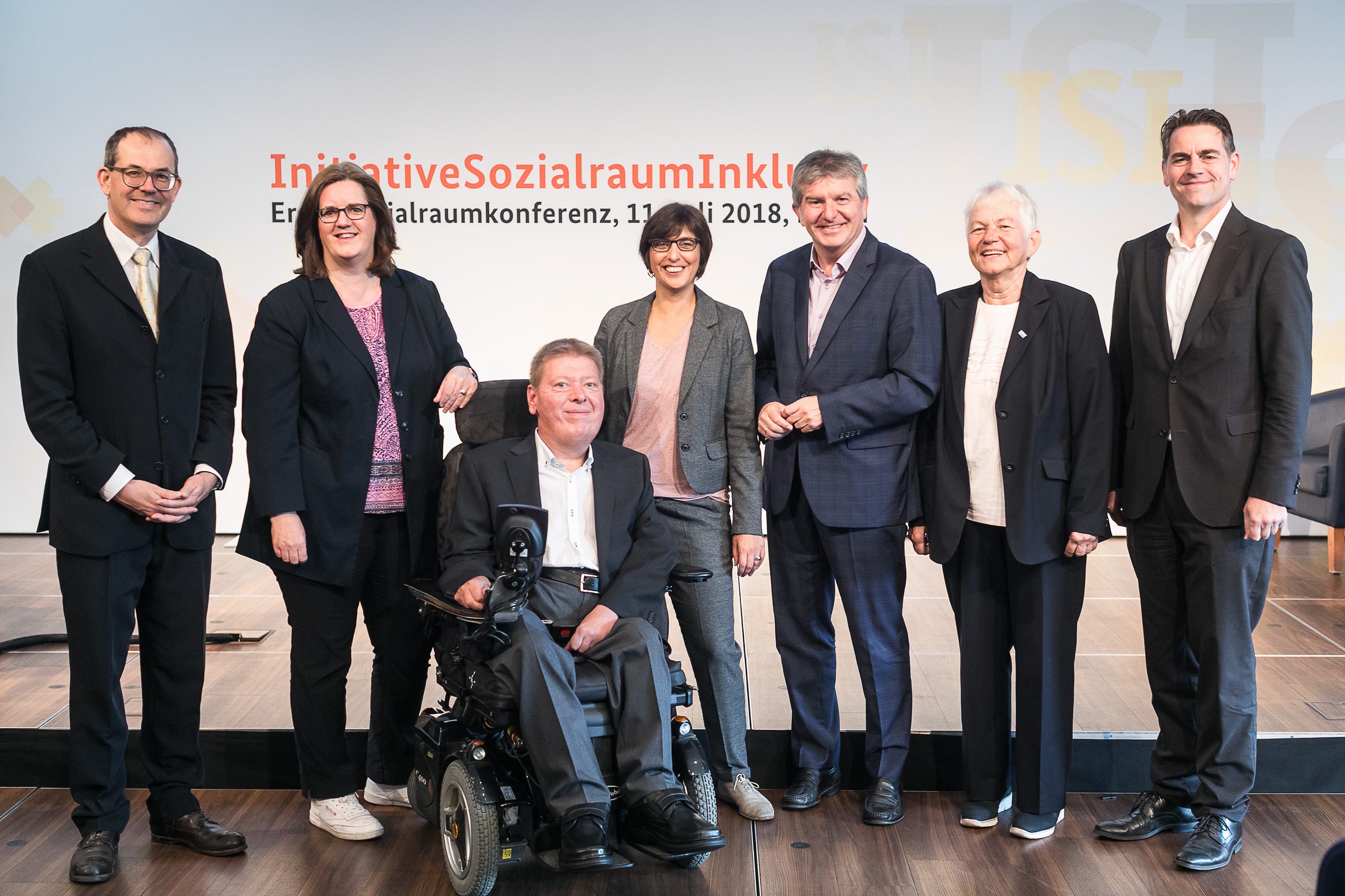 Das Bild zeigt die sieben Hauptakteure der Veranstaltung: Dr. Valentin Aichele, Kerstin Griese, Dr. Volker Sieger, Vanessa Ahuja, Peter Renzel, Renate Falk, Stefan Hahn vor der Bühne der Veranstaltung. 