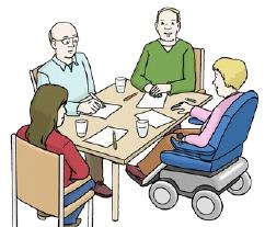 Vier Personen, davon eine mit Rollstuhl sitzen am Tisch und beraten sich. 